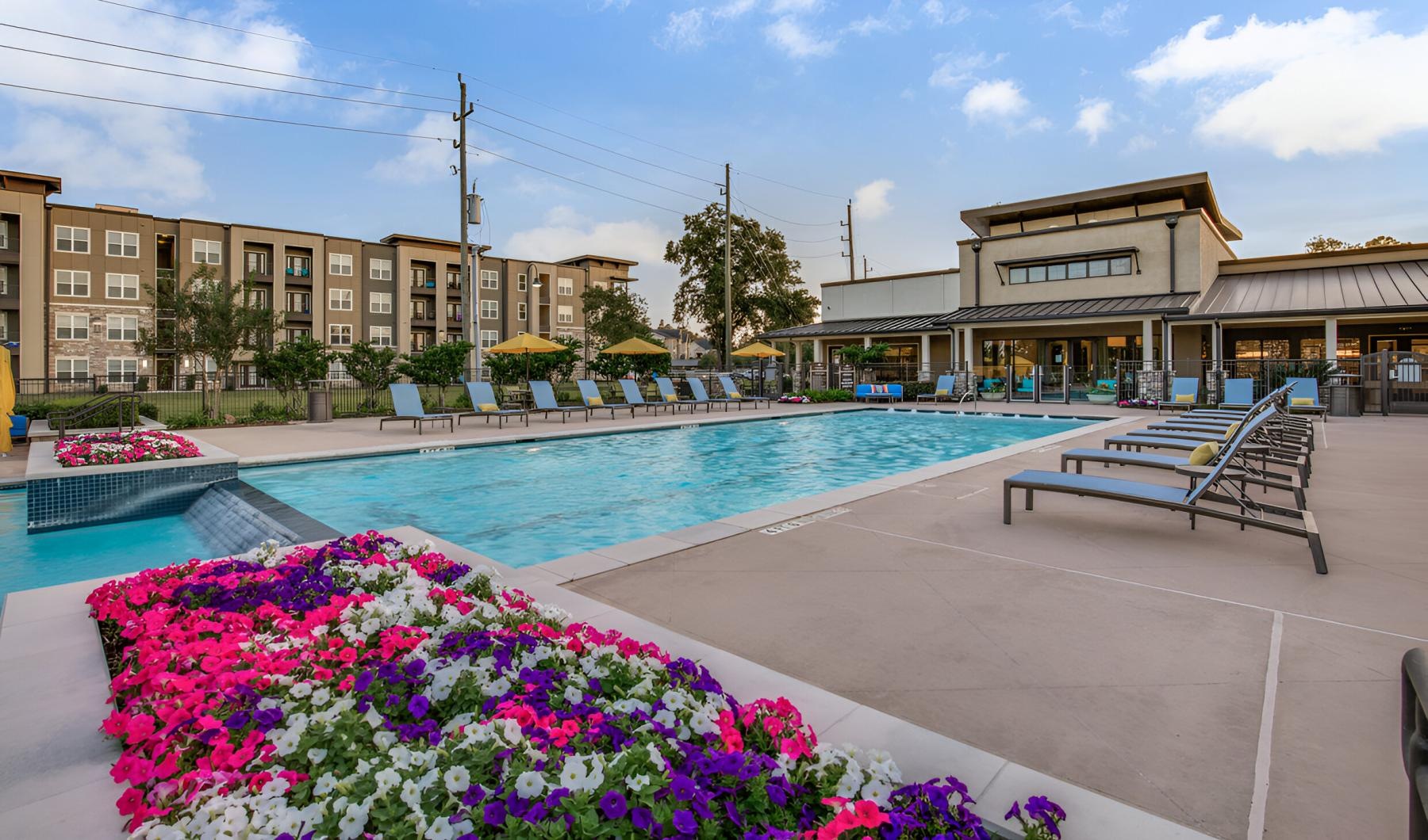 a swimming pool with flowers and a building in the background